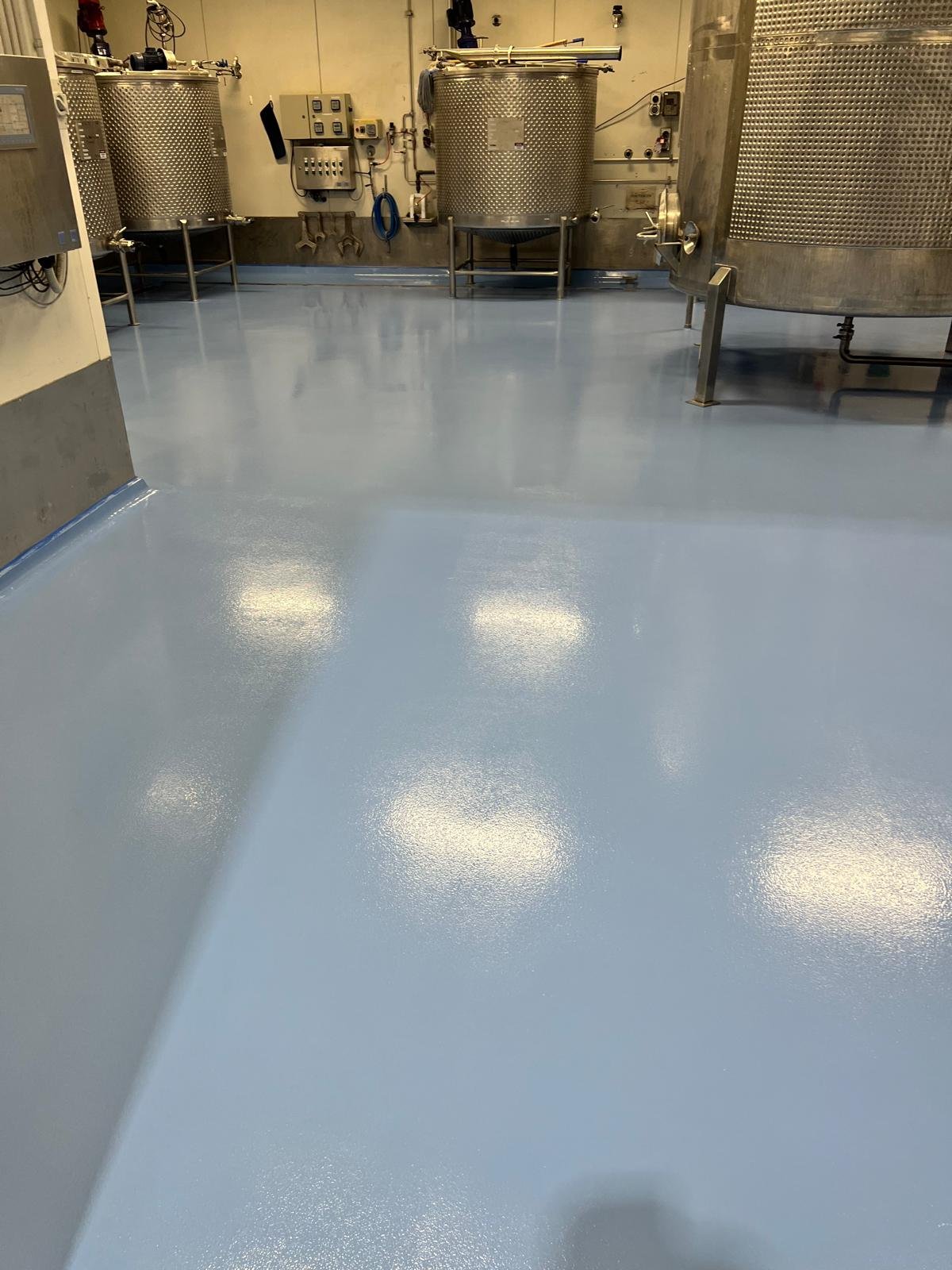 Pale blue epoxy floor between stainless tanks in a processing facility