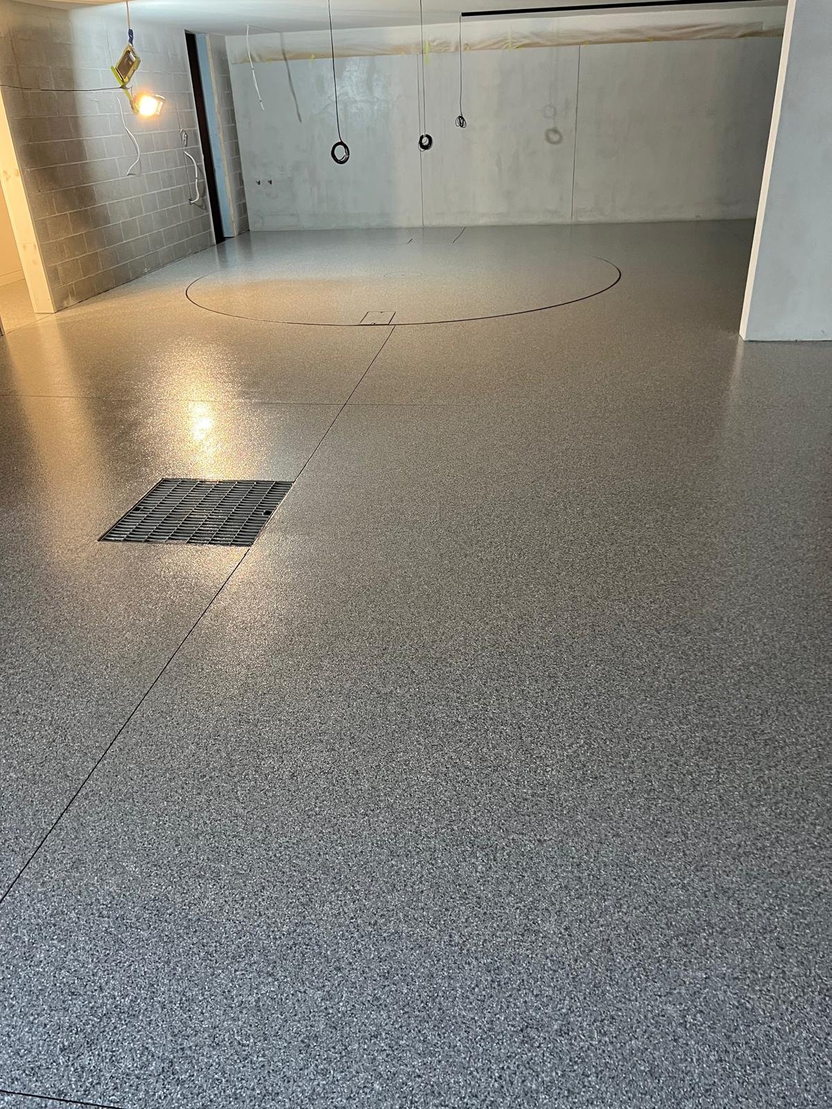 Grey epoxy flake floor in a basement garage with a drain grate